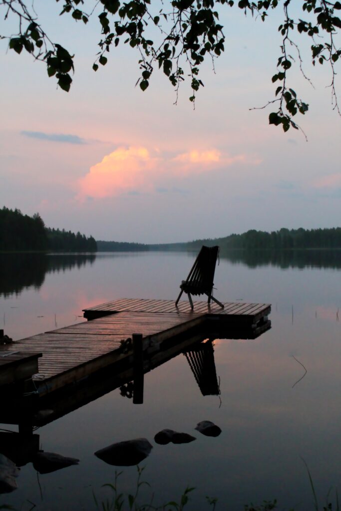 A single chair sits on the end of a dock. There is a sunset.
